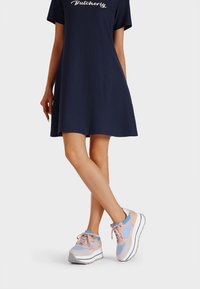 Abito navy con maniche corte e vestibilità ampia. Sneakers grigie chiare, rosa e blu con suola bianca spessa e elementi decorativi.