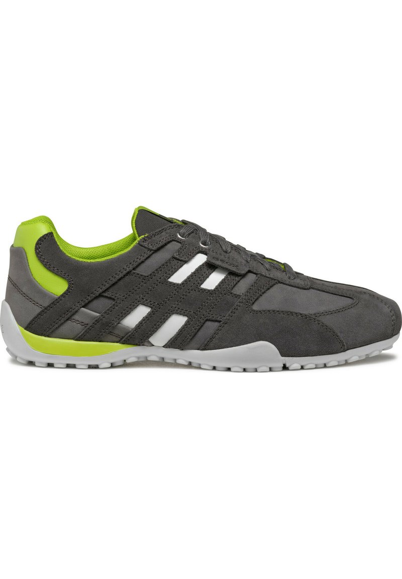 Scarpa da atletica in suede grigia con strisce bianche e dettagli verdi. Presenta un profilo basso e una suola in gomma testurizzata per una migliore aderenza.