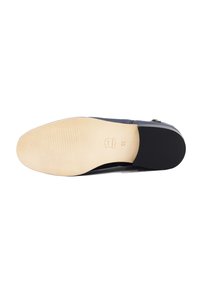 Schwarze Schuhsohle mit einem glatten, strukturierten schwarzen Gummirand und einer kontrastierenden beigen Sohle, die horizontale Rillen und ein Logo aufweist.