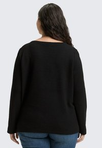Schwarzer strukturierter Pullover mit langen Ärmeln und weitem Rundhals, lockere Passform und nahtloses Design, kombiniert mit blauen Jeans.