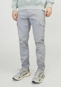 Hellgraue Cargo-Hosen mit Reißverschlusstaschen und schmalem Schnitt, kombiniert mit hellgrauen Sportschuhen aus Mesh und Gummisohlen.