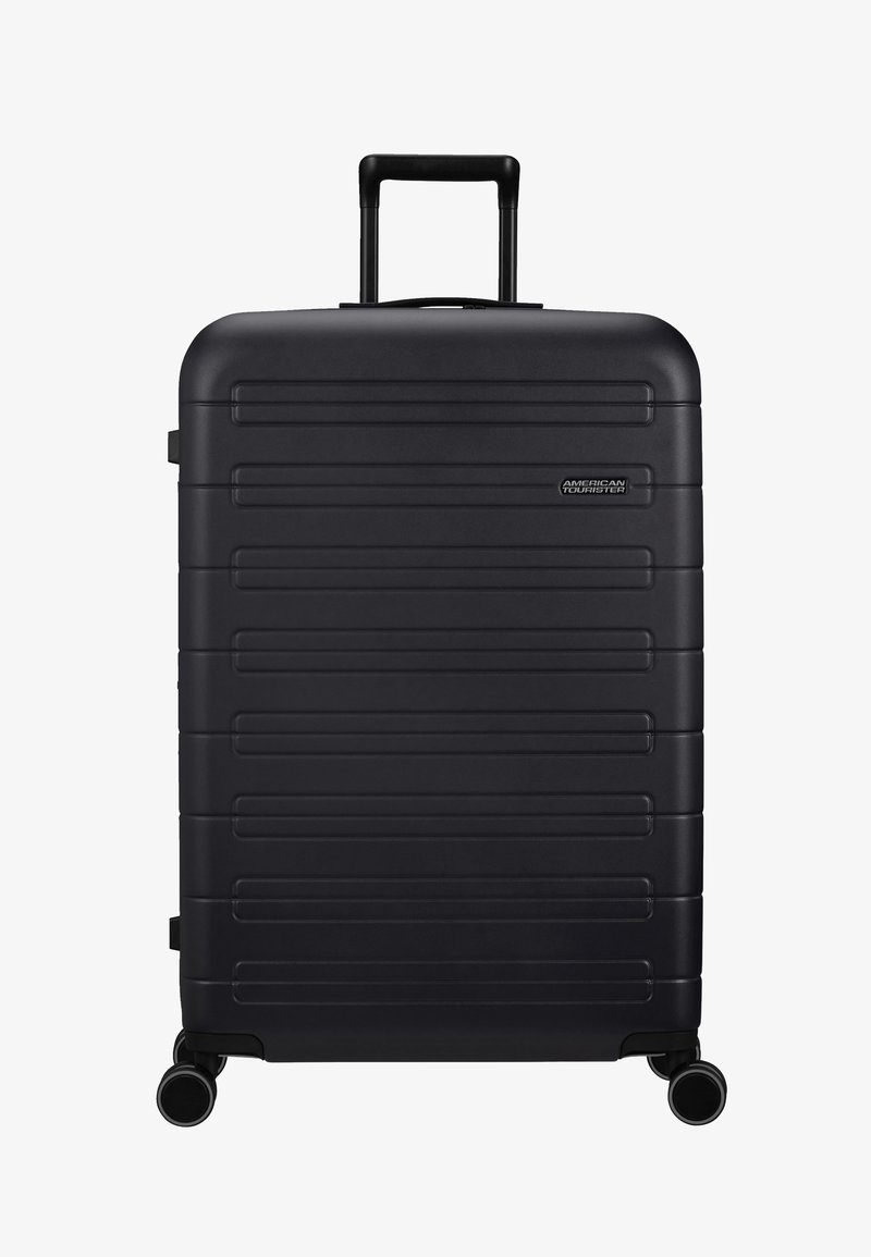 Valise en polycarbonate noir avec un design à côtes horizontales, poignée rétractable et quatre roues pour une mobilité aisée. Agrémentée du logo de la marque.