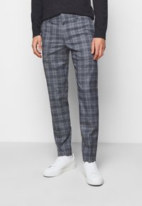 Grå rutiga byxor med en skräddarsydd passform, med ett rutig mönster och subtil textur. Kombineras med vita sneakers för en avslappnad look.