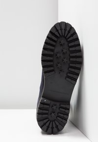 Semelle de chaussure en caoutchouc noir présentant un motif étoilé, marquée "37" et "TOMMY HILFIGER". Une matière supérieure bleu foncé est visible sur les côtés.