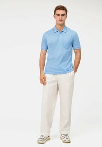 Polo di colore blu chiaro con maniche corte, colletto e taschino sul petto, abbinato a pantaloni bianchi larghi e sneakers multicolori.