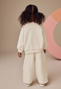 Cremefarbenes, weiches Fleece-Outfit mit einem locker sitzenden Sweatshirt und weit geschnittenen Hosen. Verfügt über gerippte Bündchen und eine lässige Silhouette.