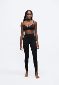 Sutien negru fără cusături și colanți cu talie înaltă. Sutienul are bretele subțiri, iar colanții au tăieturi la glezne pentru un plus de detaliu.