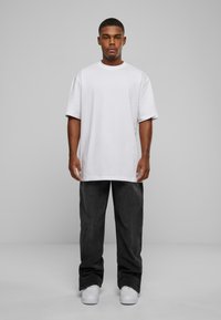 White short-sleeve t-shirt, relaxed fit, paired with loose dark gray jeans and white sneakers. Simple design, no visible patterns or graphics.