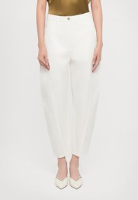 White, high-waisted, wide-leg trousers with a smooth texture, featuring subtle stitching details, and paired with pointed-toe white heels.