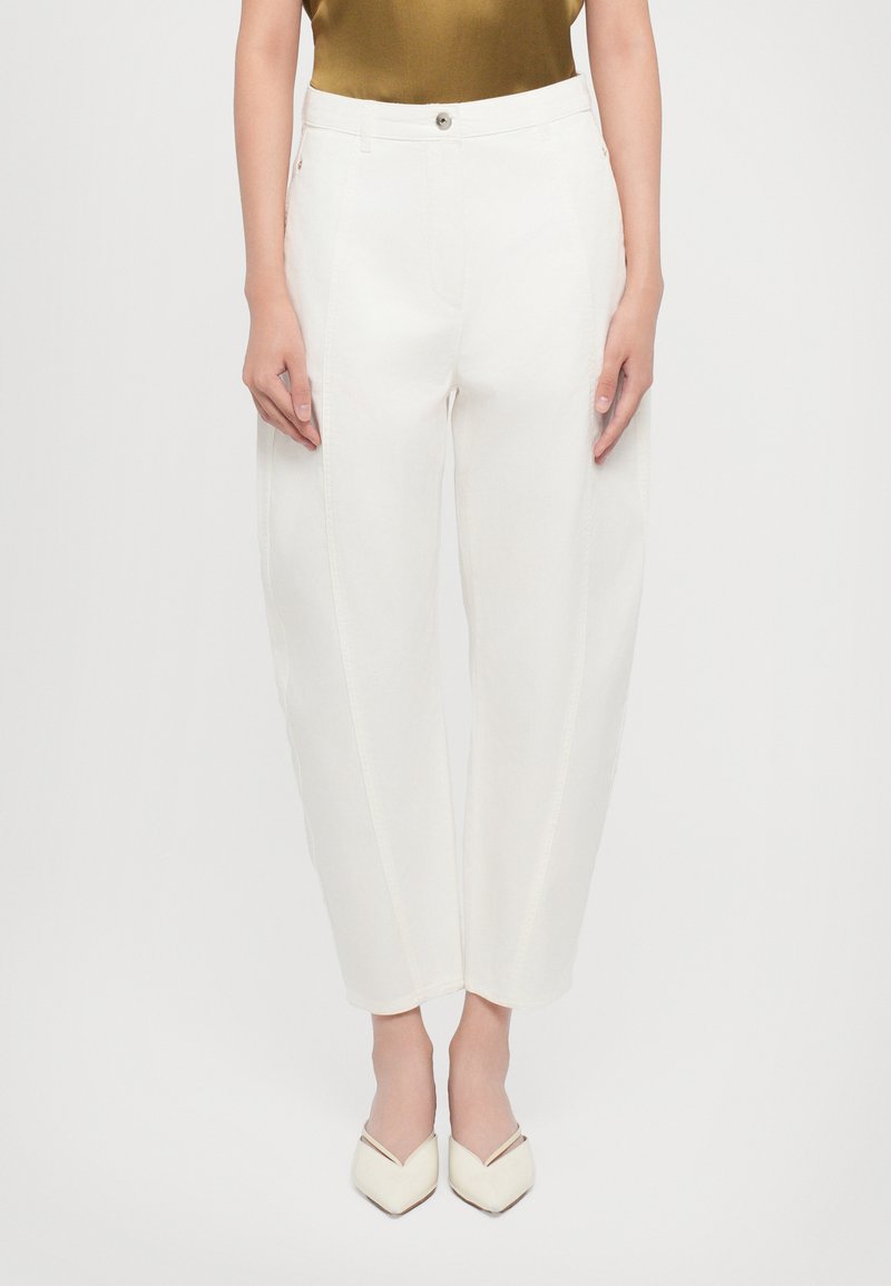White, high-waisted, wide-leg trousers with a smooth texture, featuring subtle stitching details, and paired with pointed-toe white heels.