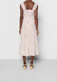 Blommönstrad midiklänning i mjuk rosa, med smockad rygg, volangärmar och lager av volanger, kombinerad med gröna klacksandaler.