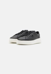 Czarne skórzane sneakersy z zaokrąglonym noskiem, płaską białą podeszwą i sznurowanym zapięciem; zawierają subtelne detale przeszycia oraz akcent w postaci logo.