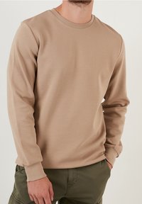 Camicia beige a maniche lunghe con texture a coste e scollo rotondo, realizzata in tessuto morbido, abbinata a pantaloni cargo verde scuro.