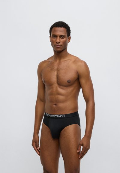 Zwarte katoenen slips met een elastische tailleband met merkopdruk, een nauwsluitende pasvorm en een gladde textuur. De stof lijkt rekbaar en zacht te zijn.