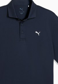 Μπλε σκούρο πόλο μπλουζάκι με γιακά, ανοίγματα με δύο κουμπιά και λευκό κεντητό λογότυπο στο αριστερό στήθος. Λείο, διαπνέον ύφασμα.