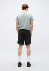 Grå kortärmad skjorta kombinerad med svarta shorts. Modellen bär vita strumpor med svarta detaljer och svarta sportskor. Enkel design, avslappnad passform.