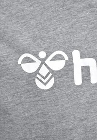 Weißes stilisiertes Bienenlogo mit geometrischen Formen und einem teilweisen Kleinbuchstaben „h“ auf grauem Stoffhintergrund.