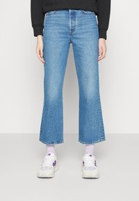 Jeans de talle alto de mezclilla de color azul claro, con acampanado, dobladillo sin rematar y textura desgastada. Combinados con zapatillas blancas con detalles en morado.