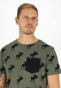 Olive green t-shirt featuring black moose patterns, round neck, and a black pocket on the left chest. Soft fabric with a smooth texture.