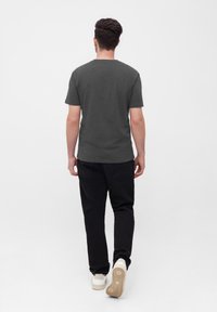 Kurzärmeliges, dunkelgraues T-Shirt mit klassischem Rundhalsausschnitt, kombiniert mit schwarzen Hosen und weißen Sneakers, von hinten betrachtet.