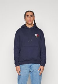 Sudadera azul marino de tejido suave con bolsillo frontal, capucha ajustable con cordón, y gráfico de rosa bordado en rojo y blanco.