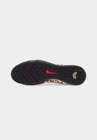 Μαύρη υφή της σόλας ενός παπουτσιού Nike με κόκκινο λογότυπο swoosh και μπεζ λεπτομέρεια σε σχήμα κεβρόν, που δείχνει το σχέδιο πέλματος σχεδιασμένο για πρόσφυση.