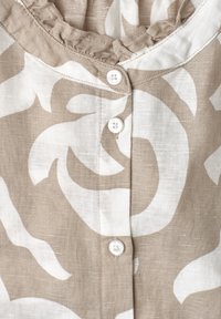 Gros plan sur un tissu beige et blanc à motifs avec trois boutons blancs et un bord de col froncé.