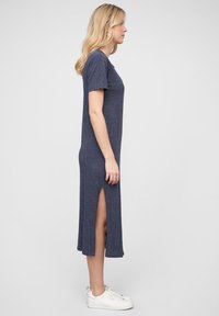Tengerészkék midi ujjatlan ruha rövid ujjal, magas oldalsó hasítékokkal, sima textúrával és kényelmes szabással. Fehér sportcipővel viselve.
