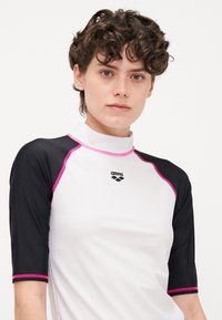 Vit simtröja med svarta korta ärmar, rosa accentstygning och hög krage. Har "arena"-logotypen på bröstet.