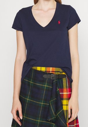 Granatowa koszulka z krótkim rękawem i dekoltem w serek, wykonana z bawełny, z małym czerwonym logo. W połączeniu z wielokolorową spódnicą w kratę i czarnym paskiem.