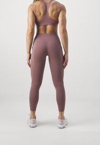 Completo sportivo con un reggiseno sportivo fitted senza maniche di un rosa scuro e leggings abbinati a vita alta con tasche laterali, abbinati a scarpe da ginnastica bianche.