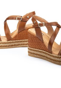 Sandalias de cuña de cuero marrón con correas cruzadas, que cuentan con una suela intermedia de yute trenzado y una suela exterior de goma texturizada para mayor agarre. Acentos de hebillas en tono plateado.