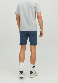 Szary i biały w paski t-shirt z krótkim rękawem w połączeniu z ciemnoniebieskimi szortami z zawiniętym dołem. Model nosi białe trampki i wzorzyste skarpetki.