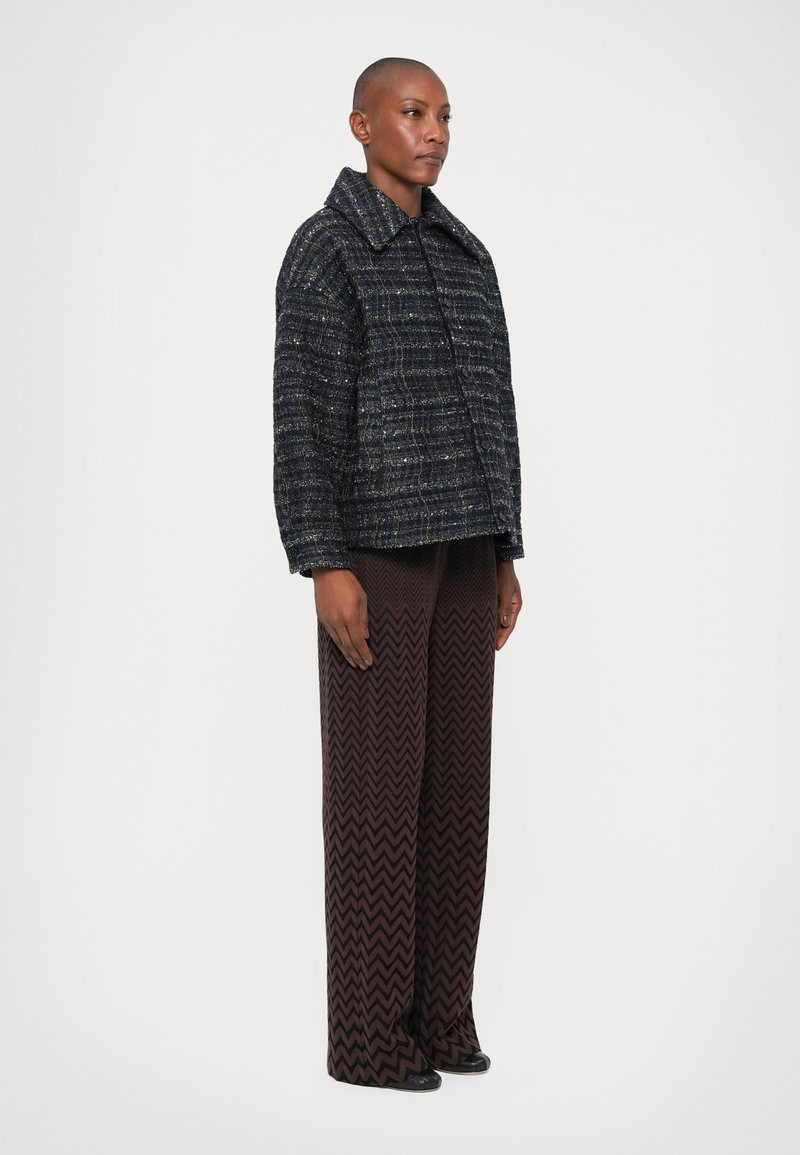 Tweedjacke in Marineblau mit dezenten metallischen Fäden, ausgestattet mit einem breiten Kragen, kastiger Form und frontaler Knopfverschluss. Stilisiert mit Hosen im Zickzackmuster.