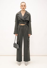 Giacca cropped grigia doppiopetto con ampie rever, pantaloni cargo a vita alta e una borsa grigia trapuntata. Tacchi a stiletto argentati completano l'outfit.