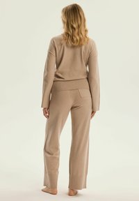 Beżowy zestaw dresowy z dzianiny, składający się z luźno dopasowanej bluzki z długim rękawem oraz spodni z szerokimi nogawkami, z prążkowanym paskiem w talii i subtelnymi kieszeniami bocznymi.