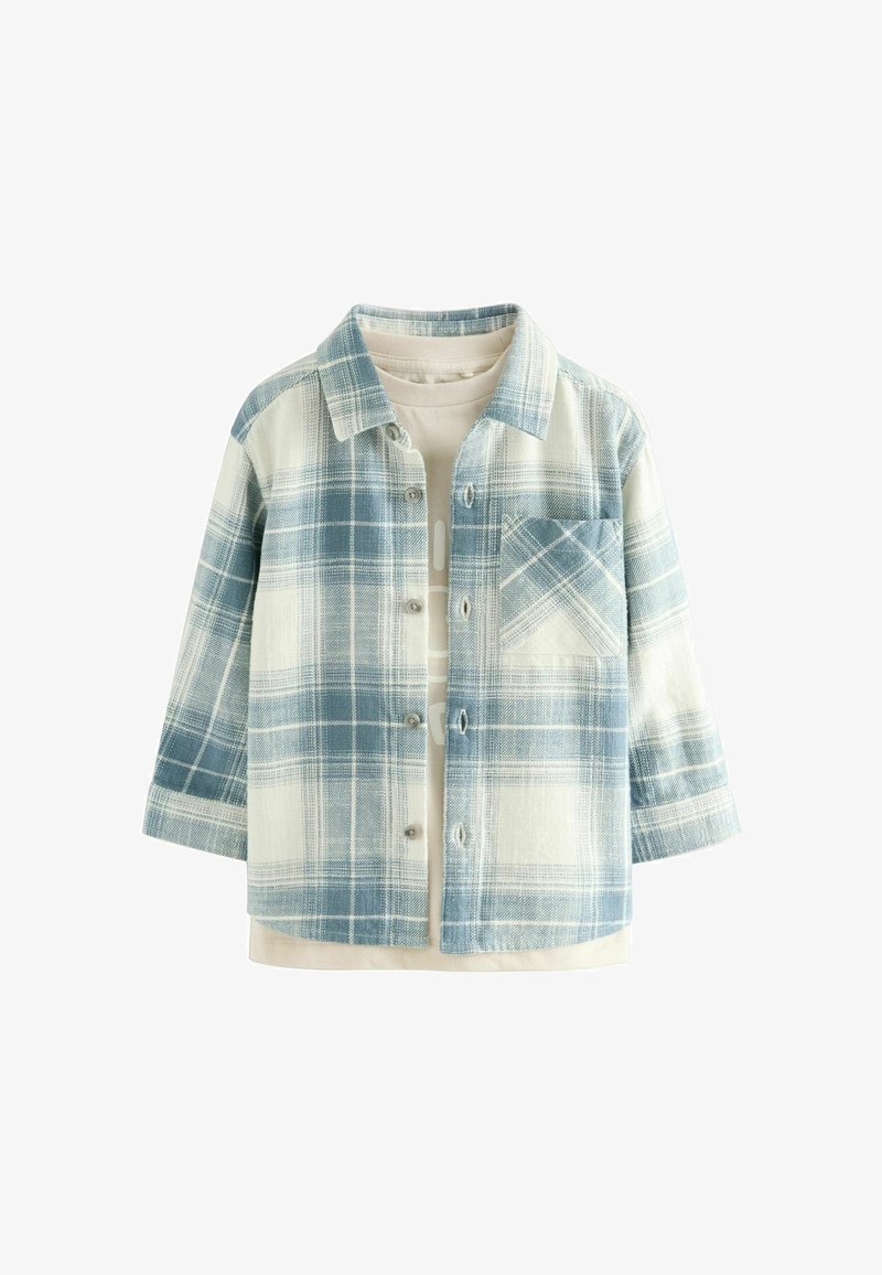 Veste à carreaux bleue et blanche boutonnée avec manches longues portée sur une chemise beige à col rond.