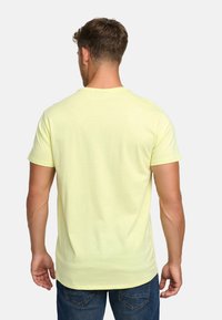 Helles gelbes T-Shirt mit Rundhalsausschnitt und kurzen Ärmeln, aus weichem Material, kombiniert mit blauen Jeans, von hinten betrachtet.