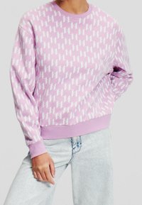 Lila sweatshirt med vitt geometriskt mönster, rund halsringning, ribbade muddar och fåll, tillverkad av mjukt material. Använd tillsammans med ljusblå jeans.