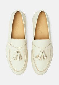 Weiße Lederloafers mit glatter Oberfläche, die an der Vorderseite eine dekorative Quaste und kontrastierende Nähte entlang der Kante aufweisen.