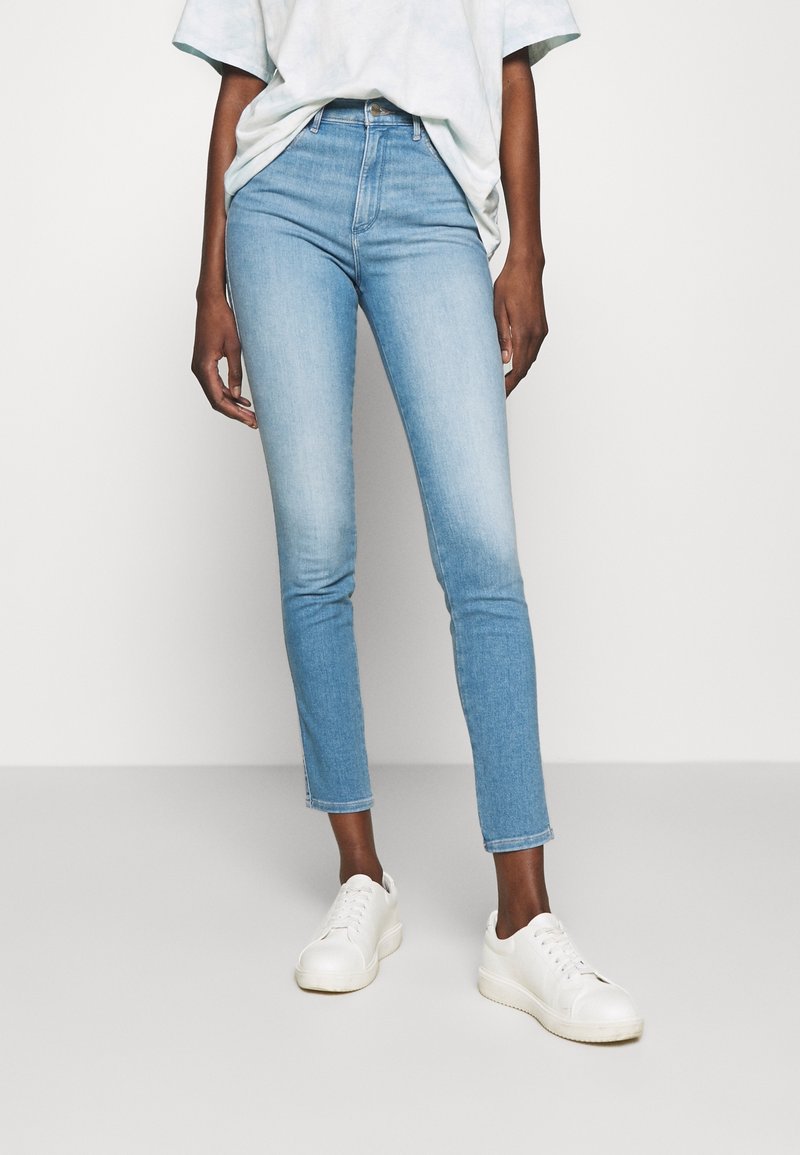 Ljusblå högmidjade skinny jeans i denim, med en blekt tvätt, ren fåll och ihop med vita sneakers.