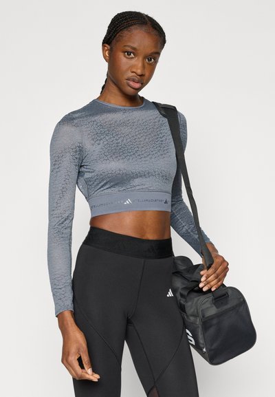 Μπλούζα με μακριά μανίκια, κοντή, υφασμάτινη γκρι με εφαρμοστή σχεδίαση, σε συνδυασμό με ψηλόμεσα μαύρα κολάν. Μαύρη τσάντα με λουρί.