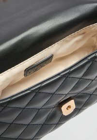 Indvendig på den sorte quiltede lædertaske er der en glat beige foring, med et guldsquare spænde og mærkets label.
