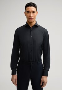 Maglietta nera a maniche lunghe con colletto a bottoni, realizzata in tessuto liscio. Caratterizzata da una vestibilità slim e bottoni neri, abbinata a pantaloni scuri.