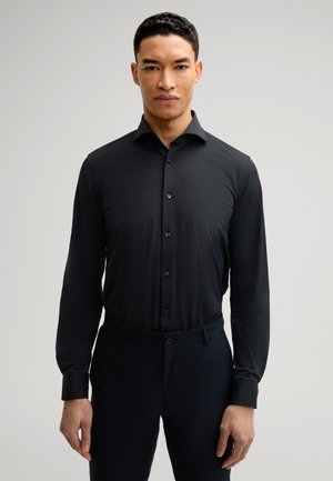 Black long-sleeve shirt with a button-down collar, made from smooth fabric. Features a slim fit and black buttons, paired with dark pants.