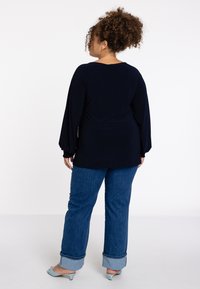 Donkerblauwe longsleeve met wijd uitlopende mouwen, gecombineerd met rechtlopende denim jeans met opgerolde boorden en open teen blauwe hakken.