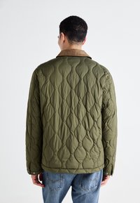 Quilted olive green jacket with a brown corduroy collar, featuring wavy textures and snap-button cuffs, paired with blue denim jeans.