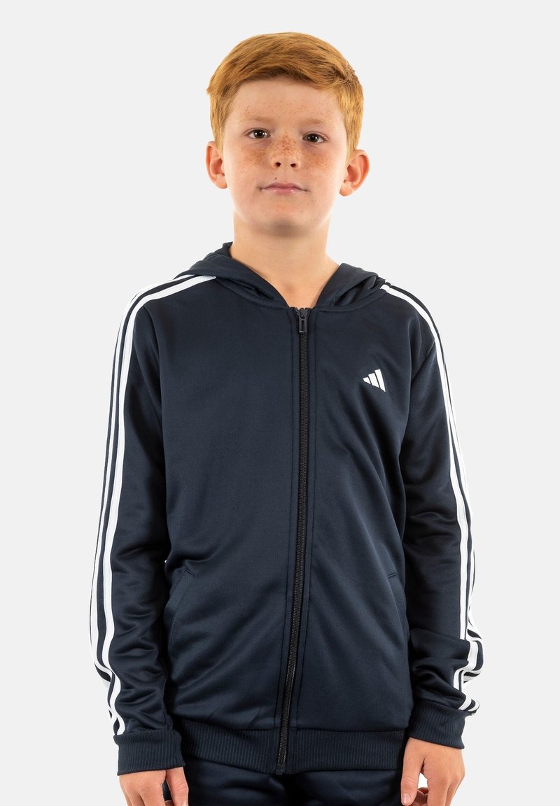 Felpa con zip color navy, con strisce bianche laterali, realizzata in tessuto morbido. Presenta una tasca frontale e un cappuccio, con un piccolo logo sul petto sinistro.