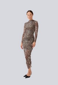 Šaty s leopardím potiskem, dlouhými rukávy a těsně přiléhající siluetou, vyrobené z průsvitné látky, se zřasenými detaily. Stylizované s černými špičatými balerínami.