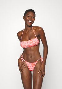 Biquíni rosa com padrão de folhas. O top apresenta um design bandeau reto com alças, enquanto a parte de baixo é de estilo com amarração lateral. Textura suave.